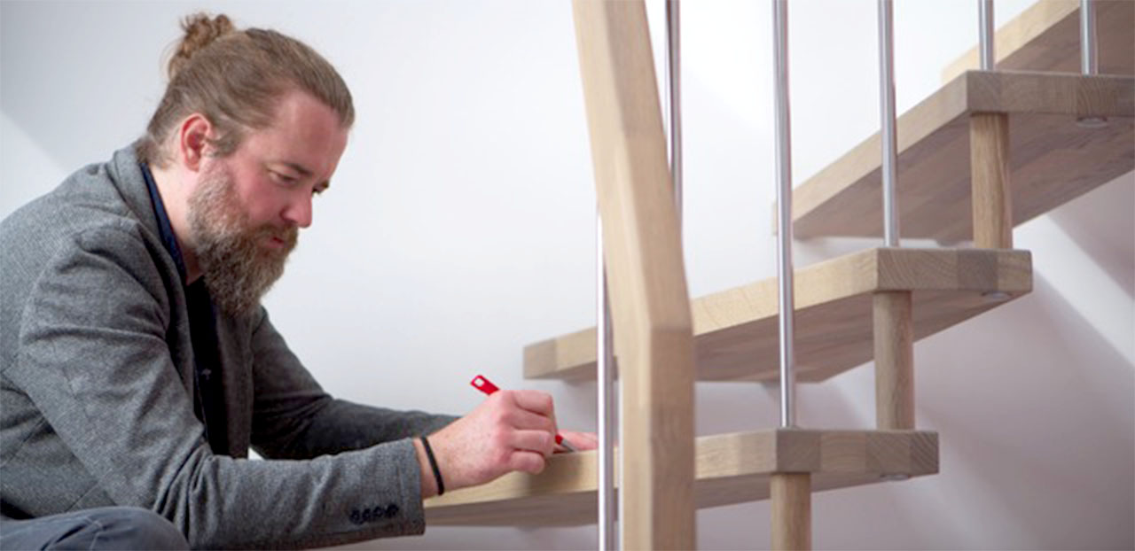 Ein Mann prüft den Zustand der Holzstufen einer hellbraunen Holztreppe